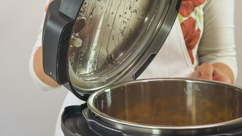A home cook opens the lid of an electric pressure cooker.
