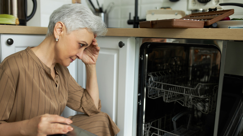 Stressed person examining a broken dishwasher.