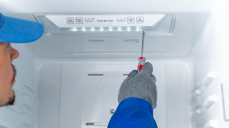 Repair person fixes freezer.