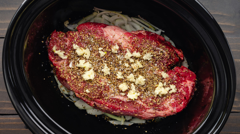 Meat atop onions inside of a Crock-Pot.