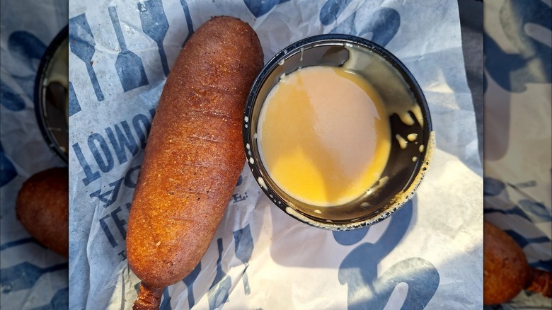 A corn dog from Culver's next to a tiny jar of cheese sauce.