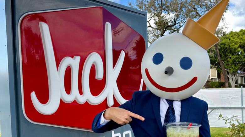 The Jack in the Box mascot stands in front of an outdoor Jack in the Box restaurant sign
