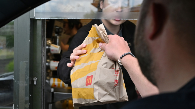 A friver receives a food bag from an employee at a McDonald's drive-thru.