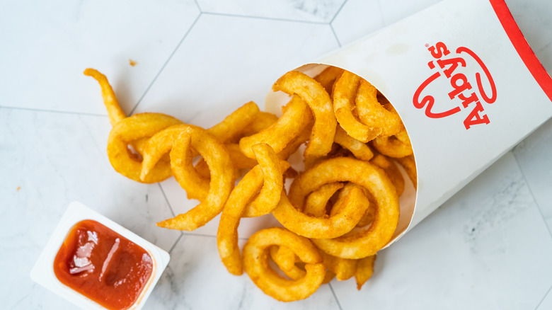 A box of Arby's curly fries is tipped on its side next to an open container of dipping sauce