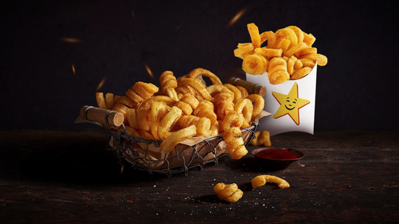 A cardboard container of Hardee's Crispy Curls sits beside a basket of the fries and a small dish of dipping sauce