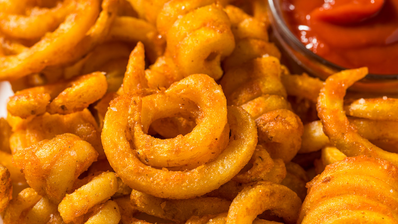 Golden curly fries are piled near a glass ramekin of ketchup