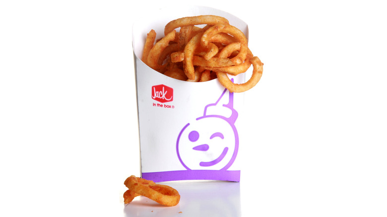 One sole curly fry sits beside a container of Jack in the Box curly fries