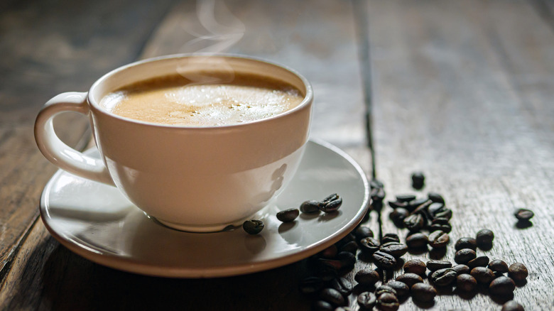 Coffee in a cup next to coffee beans.