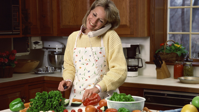 A home cook cuts vegetables in a 1990s kitchen while talking on the kitchen phone.
