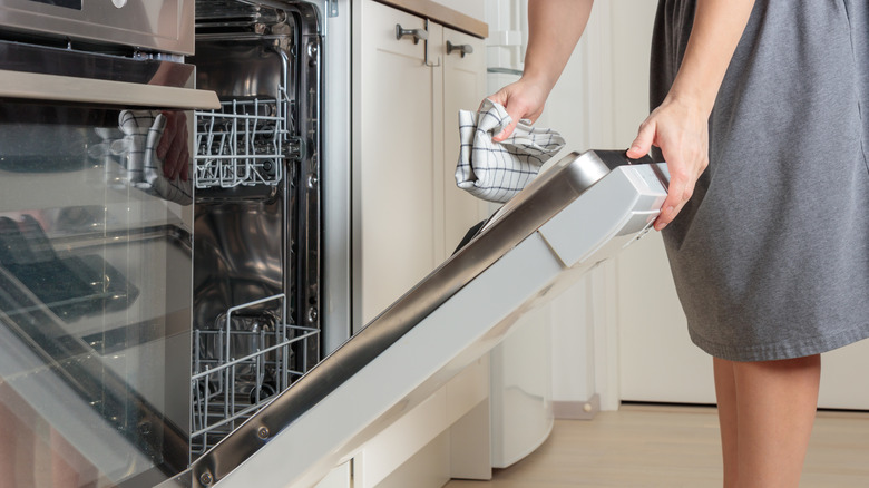 Someone's hands wipe down the interior of a dishwasher