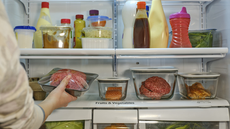 Someone selects a package of ground beef from inside an older refrigerator.