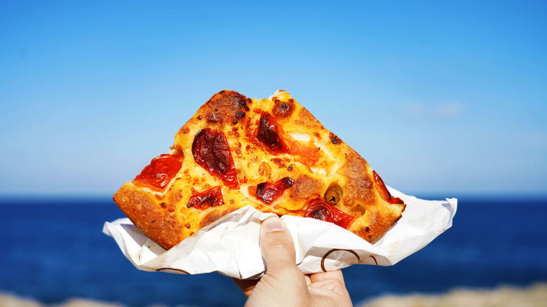 Someone holds focaccia Barese outside.