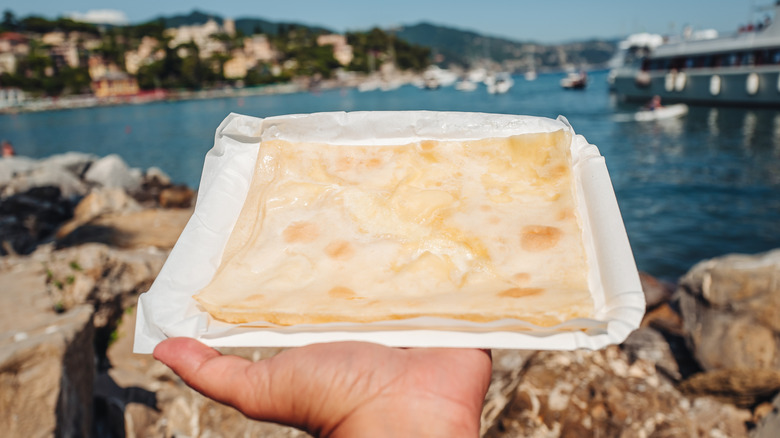 Someone holds focaccia di Recco at the seaside.