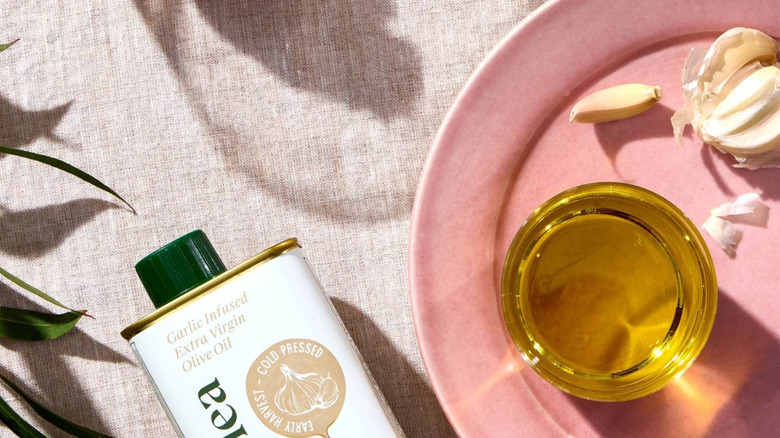 Heraclea Garlic Infused Extra Virgin Olive Oil with a bowl of oil and garlic cloves on a pink plate