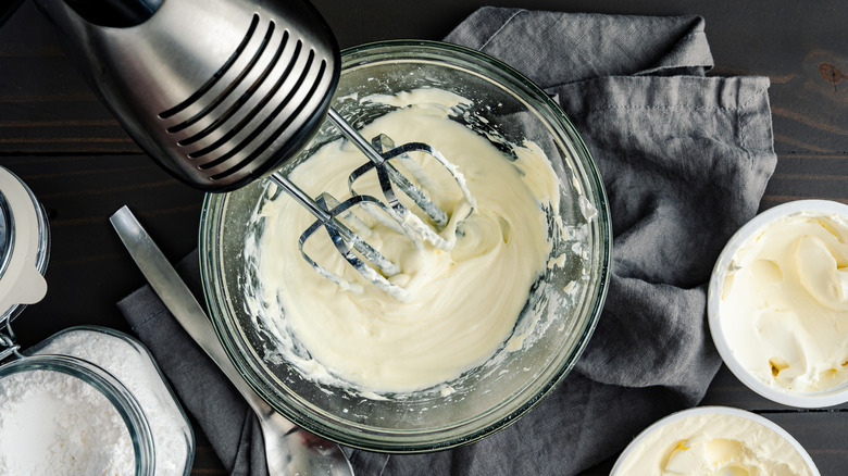 Cook turning mascarpone cream into frosting in a bowl with an electric mixer.