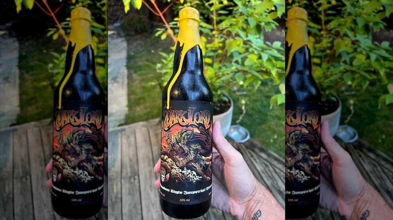 A hand holds a Three Floyds' Dark Lord Imperial Stout bottle.