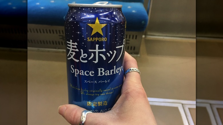A hand holds a can of Sapporo Space Barley.