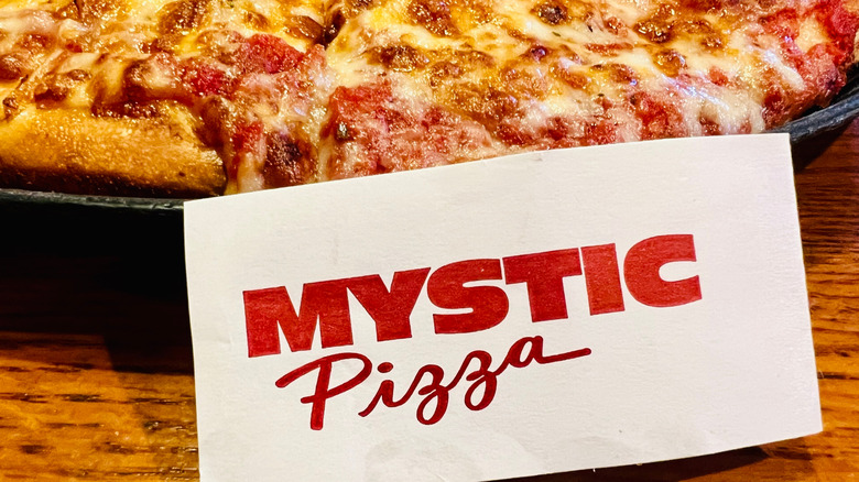 A big, cheesy pizza behind a card that reads "Mystic Pizza"