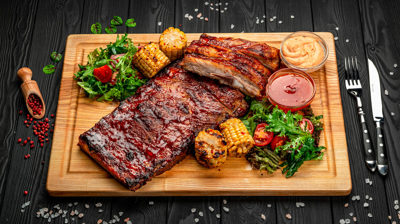 Ribs resting on a board with sides and sauces.
