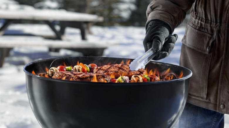 Person grilling steak and vegetables in snow