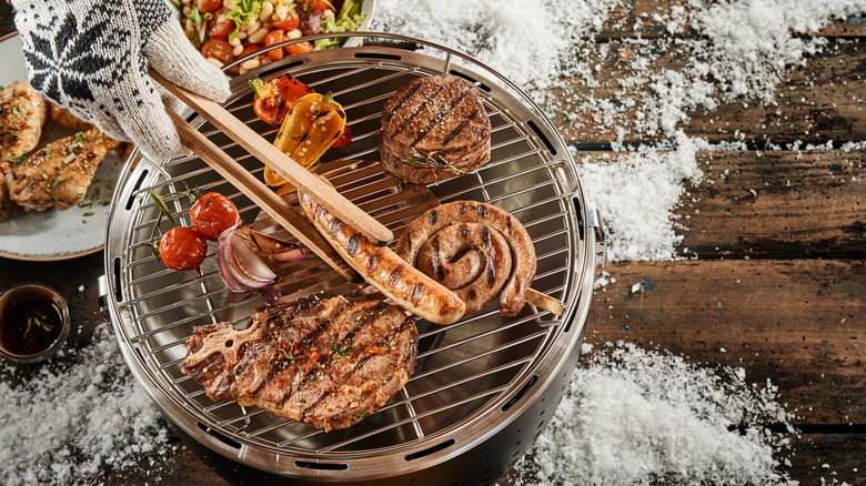 small winter grill with snow, steak, and sausages
