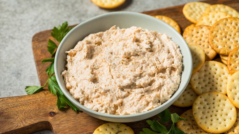 Oyster dip in a bowl next to crackers on wooden board