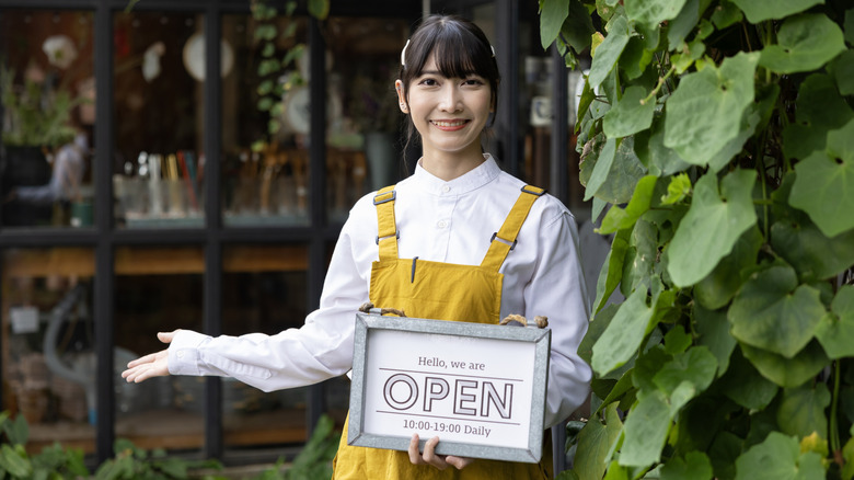 A restaurant staffer standing outside with a welcoming sign, urging customers inside.