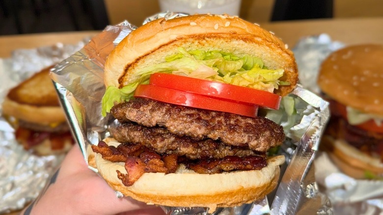 A hand holds out a loaded burger from Five Guys