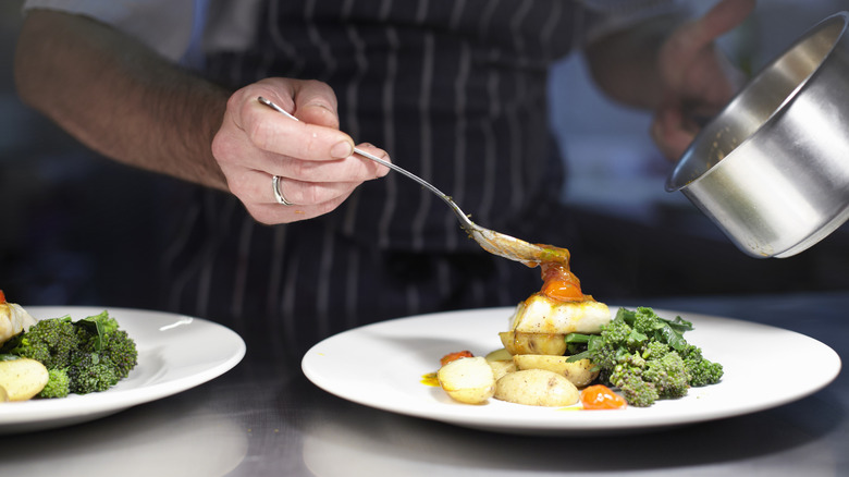 A chef spoons sauce onto a plate of vegetables