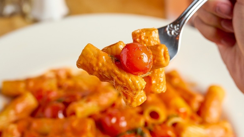 A fork holds pasta and a cherry tomato above the dish.