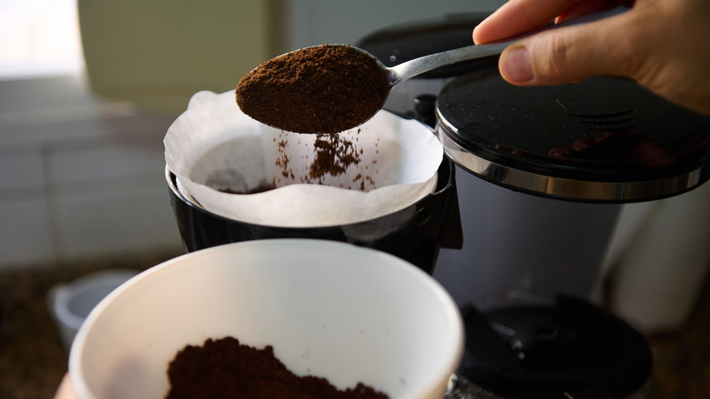 person adding coffee to a filter in a coffee pot