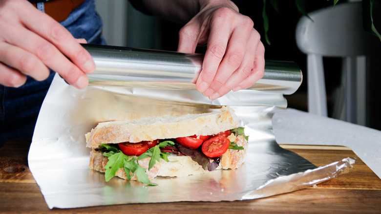 person wrapping a sandwich in aluminum foil
