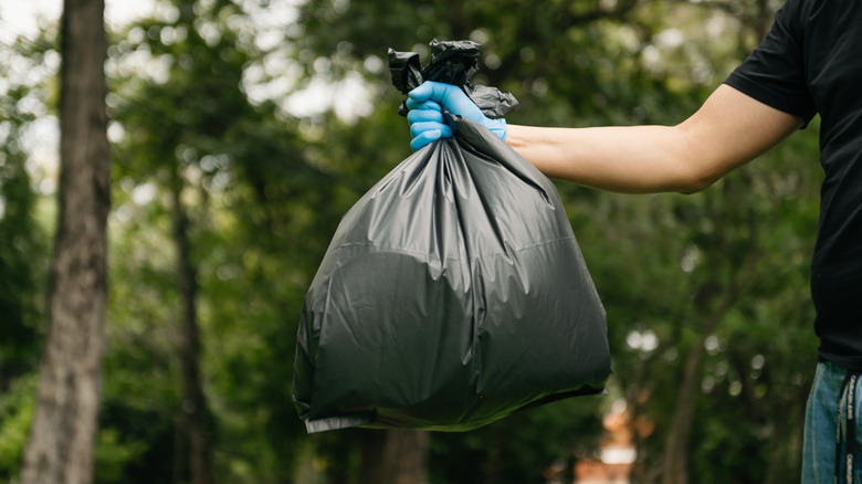 person wearing blue gloves holding back trash bag