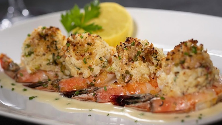 four crab stuffed shrimp on top of a buttery sauce on a plate