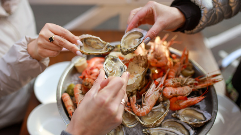 three hands holding oysters over a seafood platter