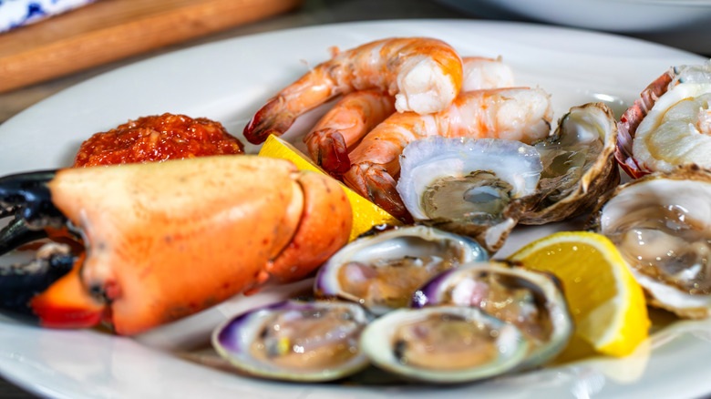 a plate of seafood with crab claw, clams, shrimp, oysters, and lemon