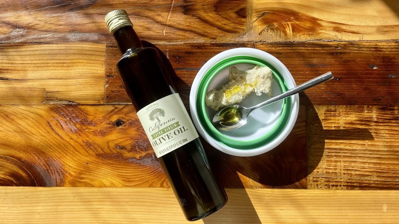 Overhead view of a bottle of Trader Joe's California Extra Virgin Olive Oil lying on a wooden table with a spoonful of the oil and a piece of bread