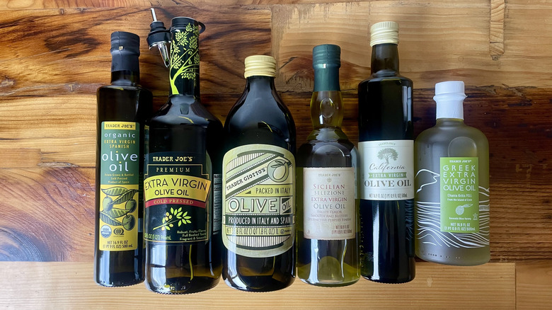 Overhead view of six different types of Trader Joe's Olive Oil lying on a wooden table top