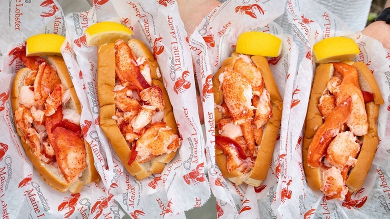 Four lobster rolls with lemon wedges at Cousins Maine Lobster