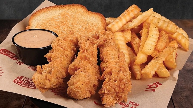 Three Huey Magoo's chicken tenders, fries, Texas toast, and dipping sauce sit on a table in the restaurant
