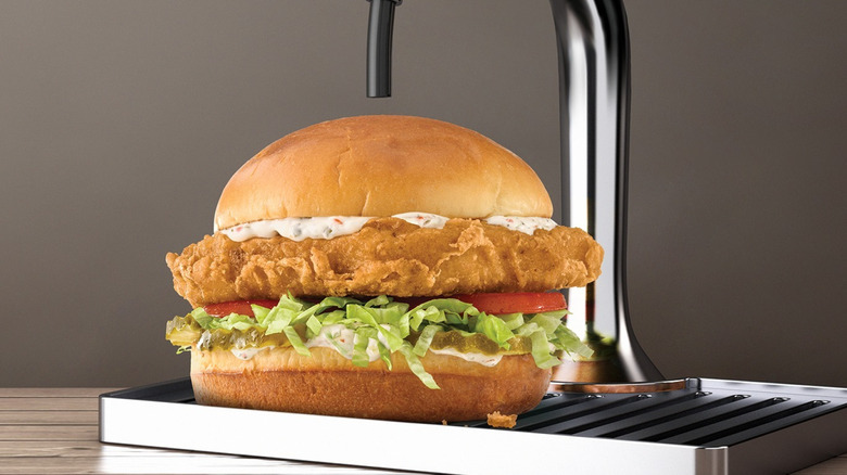A beer battered fish sandwich under a beer tap