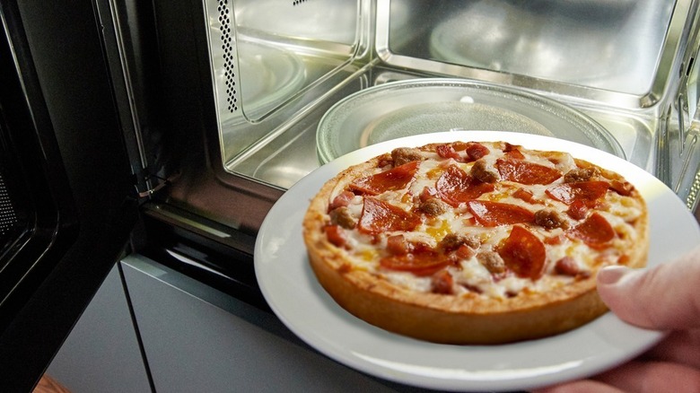 A pepperoni deep dish pizza coming out of the microwave