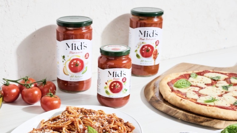 Jars of Mid's sauce with pizza, pasta, and tomatoes