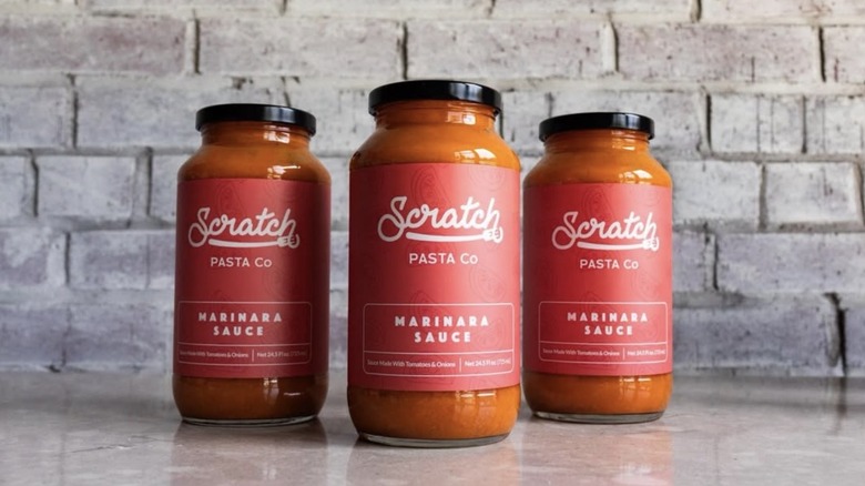 Jars of Scratch Pasta Co. marinara lined up in front of a brick wall