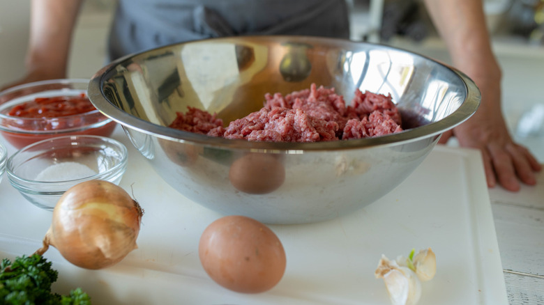 Ground beef, sauce, onion, and egg gathered to prepare meatloaf