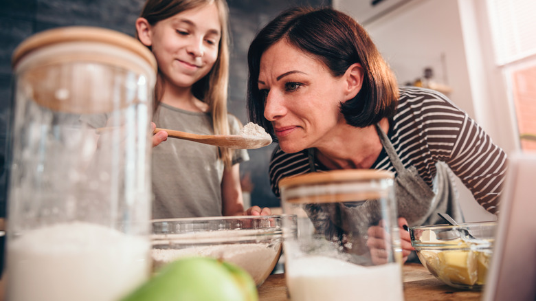 Mother smelling spoon of flour while baking with daughter