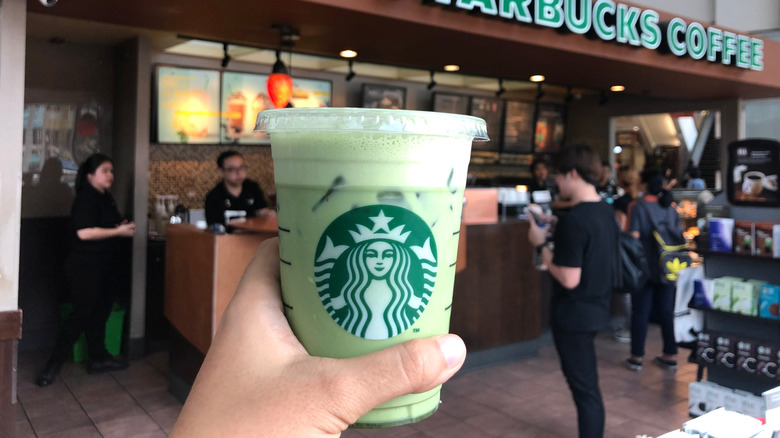 A man holds a to-go cup of Starbucks matcha latte in front of a store