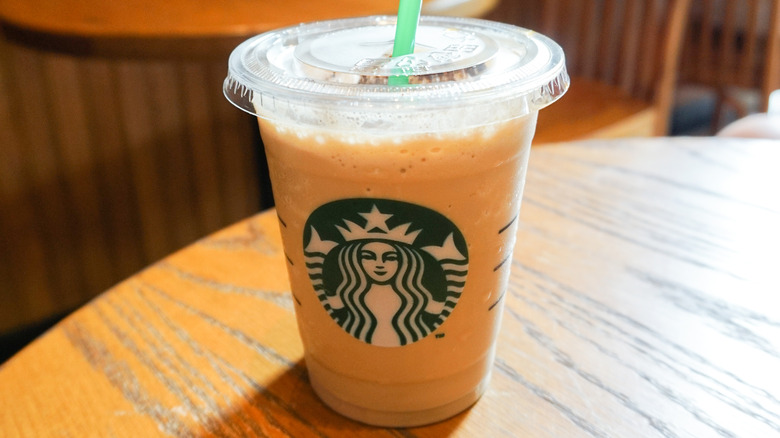 A Starbucks latte in a to-go cup sits on a wooden table bathed in sunlight