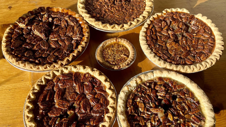 Six different store-bought pecan pies on a wooden table