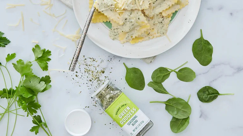 Jar of Trader Joe's Green Goddess Seasoning Blend with fresh herbs and a plate of ravioli
